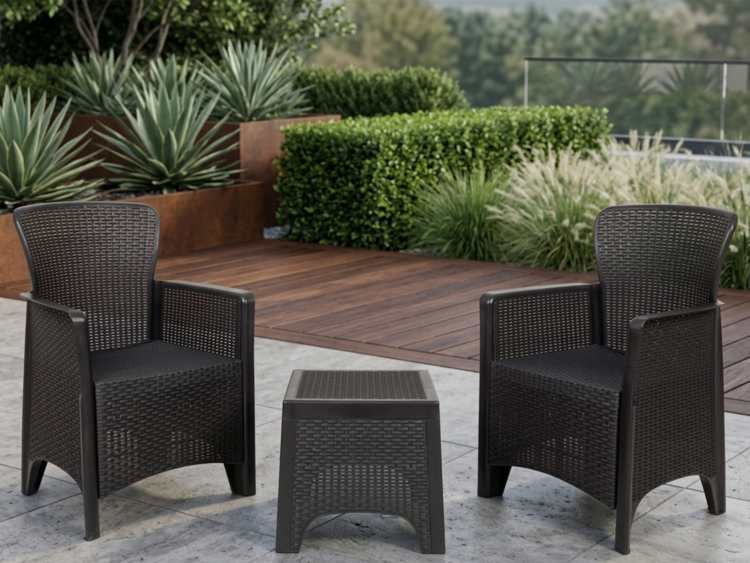 Outdoor seating area with two black wicker chairs facing a small matching table on a stone patio, with greenery in the background.