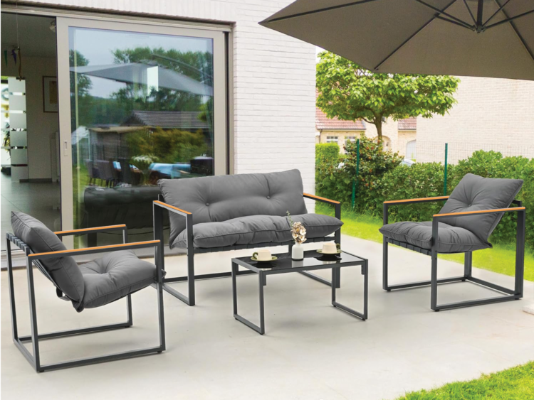 Outdoor patio seating set with gray cushions and black metal frames around a small coffee table on a concrete patio under a large umbrella.