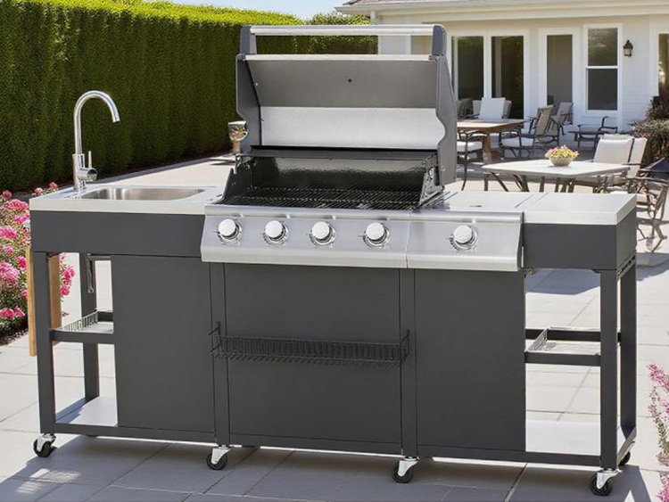 Outdoor stainless steel gas grill island with side sink on the left, mounted on wheels in a sunny backyard patio.