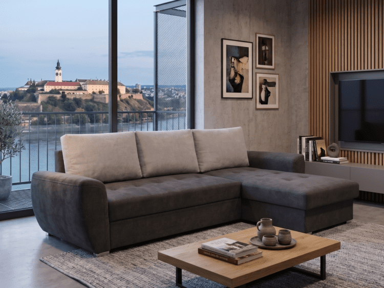 Modern living room with a gray sectional sofa, light cushions, and a wooden coffee table facing a wall-mounted TV; large windows show a river and town beyond.