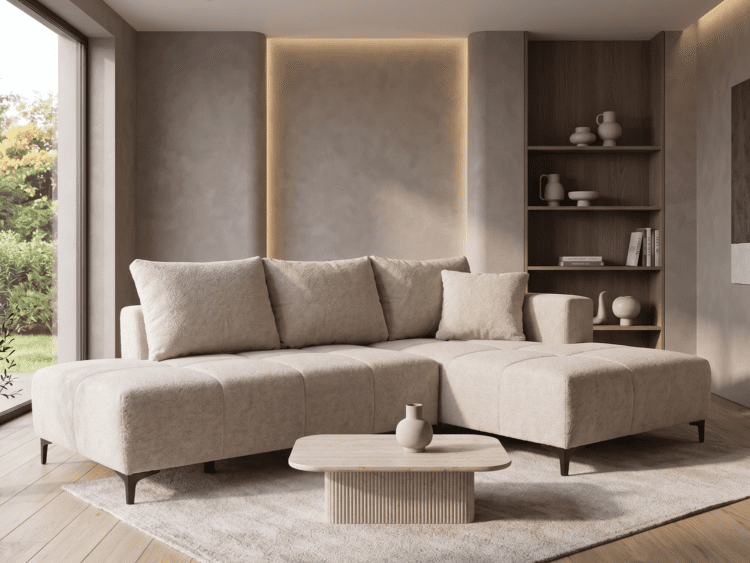 Neutral beige sectional sofa in a modern living room with a wooden bookshelf, round coffee table, and large window showing greenery outside.
