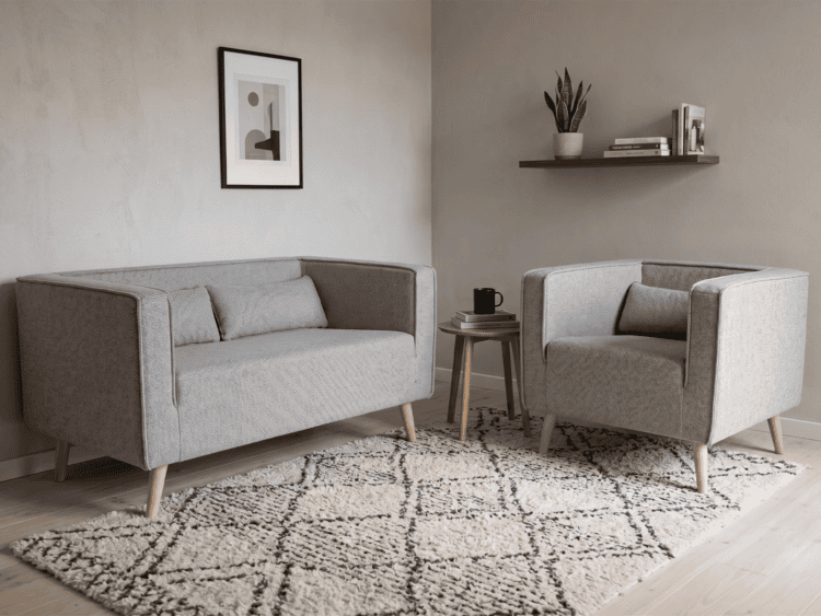 Two gray armchairs facing each other with a small round table and mug between them in a cozy living room.