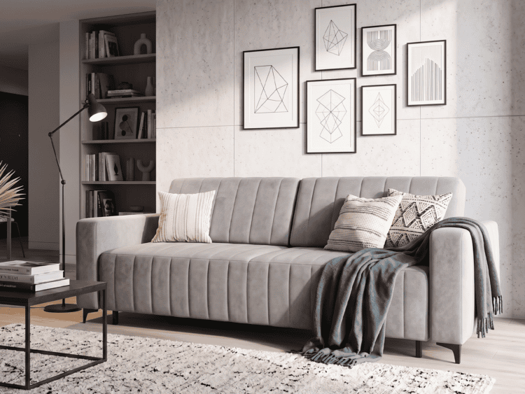 Gray tufted sofa in a contemporary living room with geometric art on a concrete wall and a cozy throw blanket on the armrest.