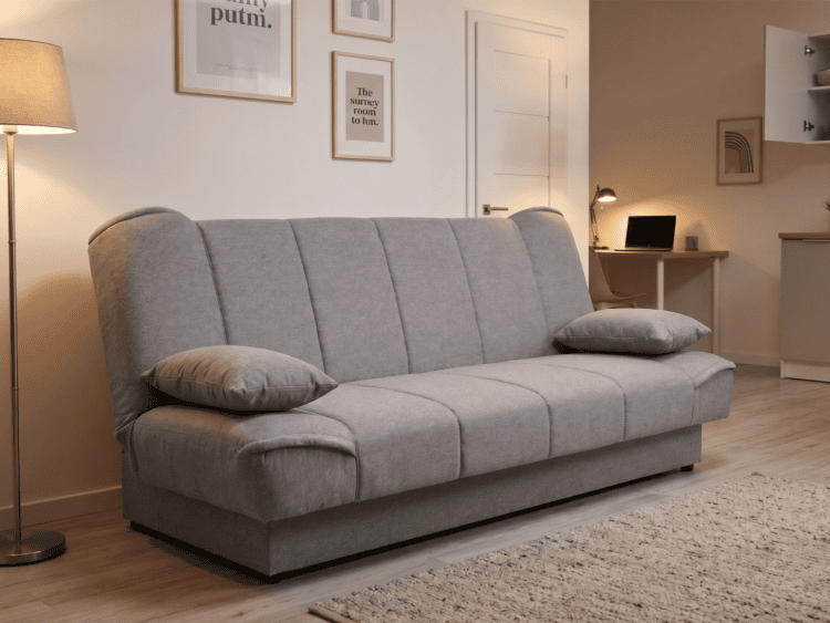 Light gray three-seat sofa with two cushions in a modern living room, rug and a desk with a laptop in the background.