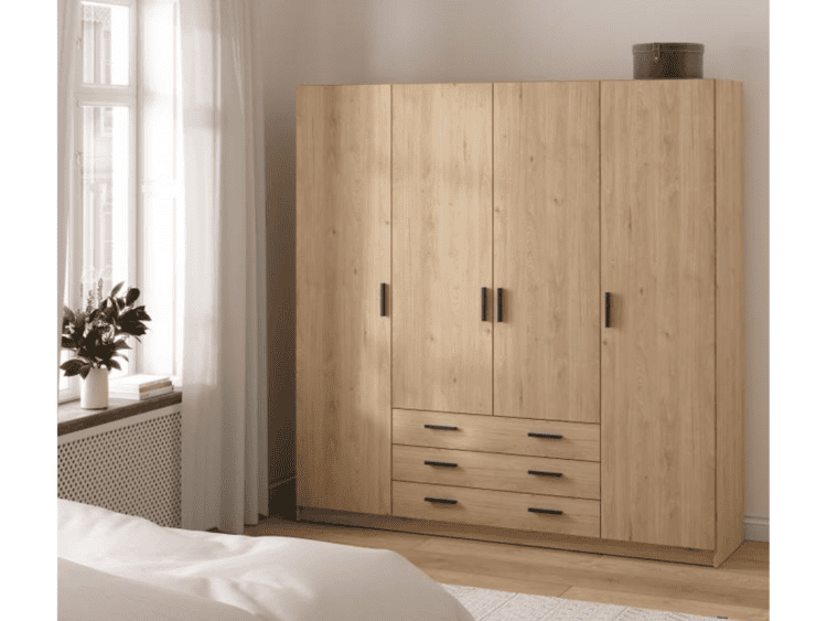 Light wood wardrobe with four tall doors and three drawers in a bedroom, topped by a dark storage box; window with sheer curtains to the left.
